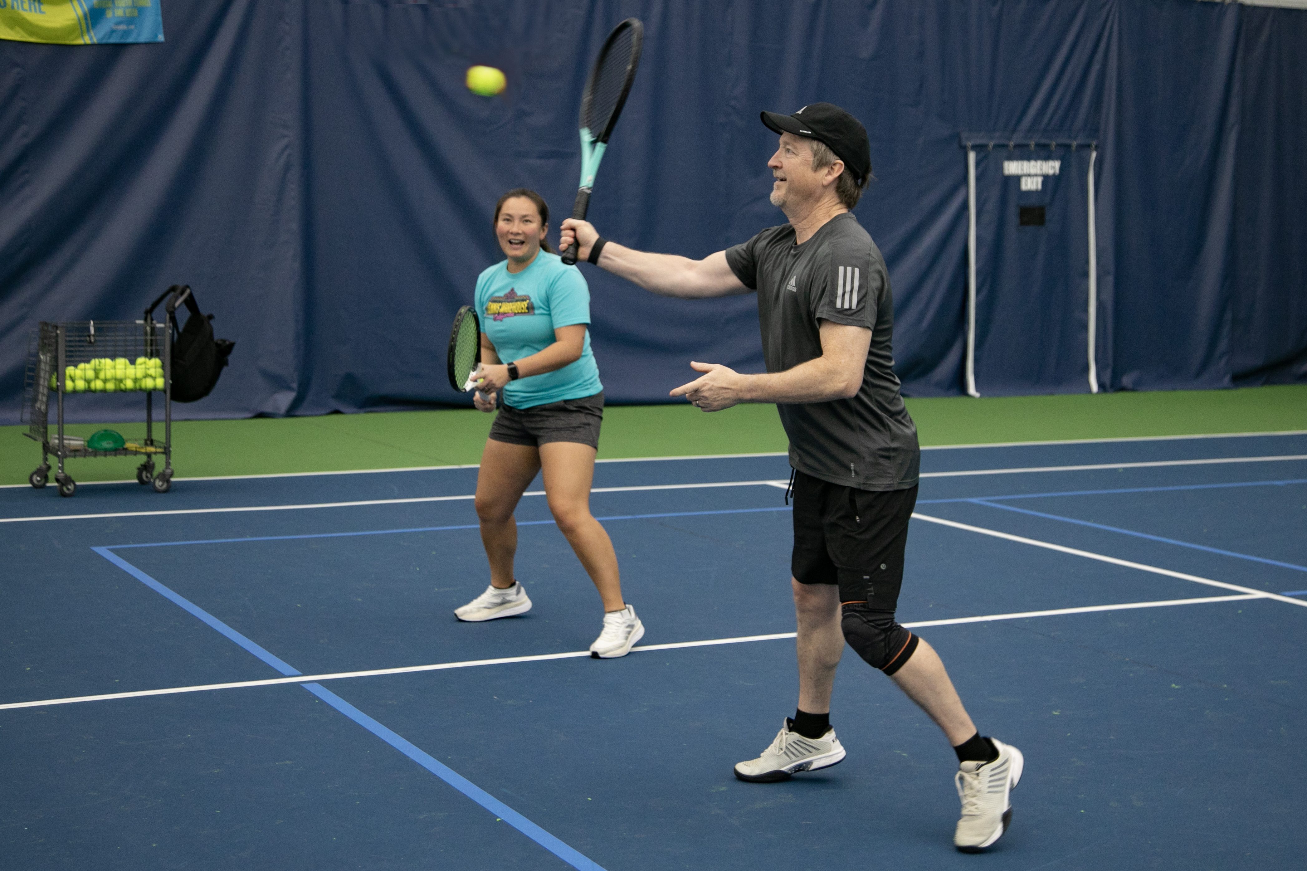 Male and female smiling, hitting a tennis ball on the tennis court.
