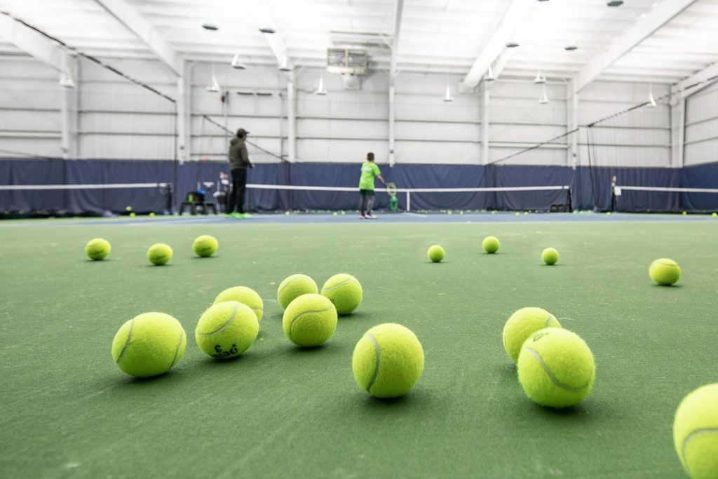 Tennis balls laying across the tennis court with two tennis players in the background.